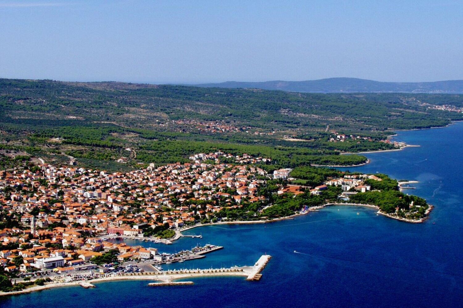 An aerial view of a coastal town with dense housing, a marina, and a prominent pier.