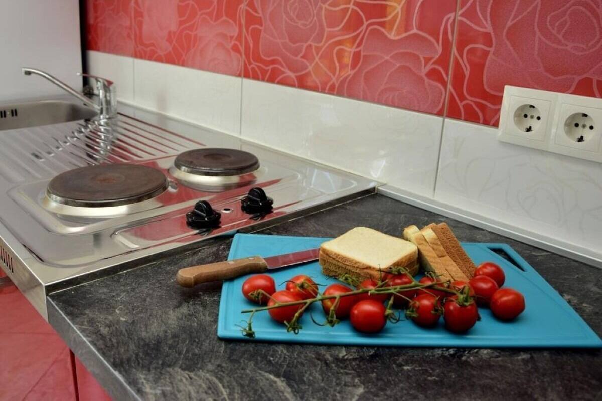 Une cuisine équipée d’une cuisinière à gaz, d’une planche à découper avec des tomates et du pain, et d’un crédence rouge et blanc.