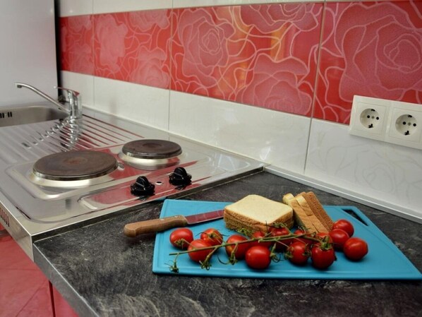 A kitchen with a gas stove, a cutting board with tomatoes and bread, and a red and white backsplash. - Apartments Vini (Trogir)