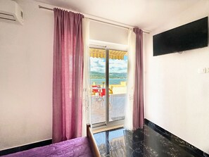 A hotel room with a sliding glass door leading to a balcony with a table and chairs, and a TV mounted on the wall. - Apartments Vini (Trogir)