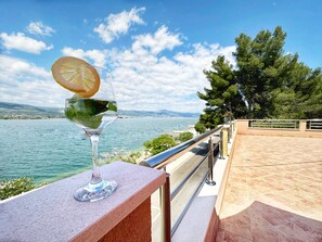 A clear view of a lake with a glass of water on a balcony, overlooking a distant shoreline with trees and a clear sky. - Apartments Vini (Trogir)