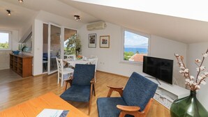 A spacious living area with a dining table, two blue chairs, a TV, and a view of the sea through large windows. - Apartment Ana (Supetar)