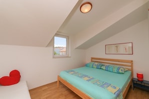 A bedroom with a sloped ceiling, a single bed, a small window, and a red heart-shaped pillow. - Apartment Ana (Supetar)