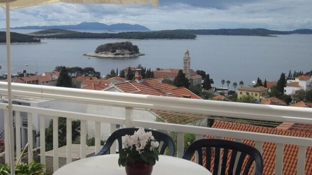 A balcony with a table and chairs, overlooking a body of water with a small island and buildings in the background. - Apartments and Room Dar (Hvar)