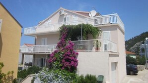 A two-story residential building with balconies, a satellite dish, and a garden with purple flowers. - Apartments and Room Dar (Hvar)