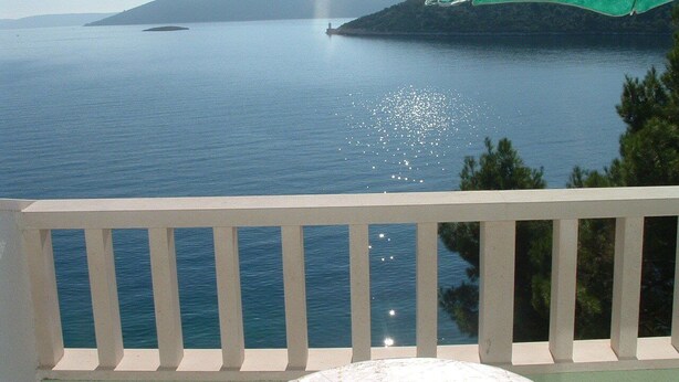 Un balcone con vista su un mare calmo e una costa lontana.