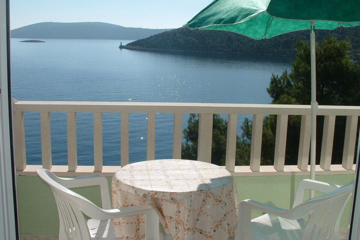 Ein Balkon mit Tisch und Stühlen, mit Blick auf ein Gewässer und eine entfernte Küste.