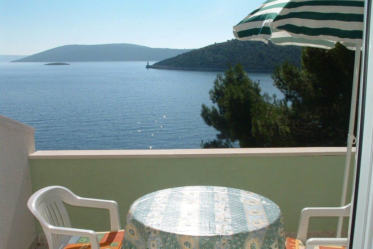 Ein Balkon mit Tisch und zwei Stühlen, mit Blick auf ein Gewässer und eine entfernte Insel.