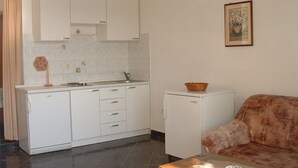 Una cucina compatta con mobili bianchi, un piccolo frigorifero e un'area pranzo con un divano decorato.