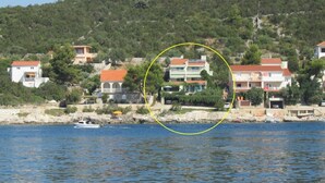 Un villaggio costiero con case lungo la riva, una barca sull'acqua e una collina ricoperta da vegetazione lussureggiante sullo sfondo.