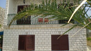 A two-story building with white brick walls, two windows with brown shutters, and a balcony with a green railing. - Apartment Smil (Sucuraj)