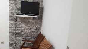 Una habitación pequeña con un televisor montado, un revestimiento de pared con diseño de piedra y dos sillas de madera.