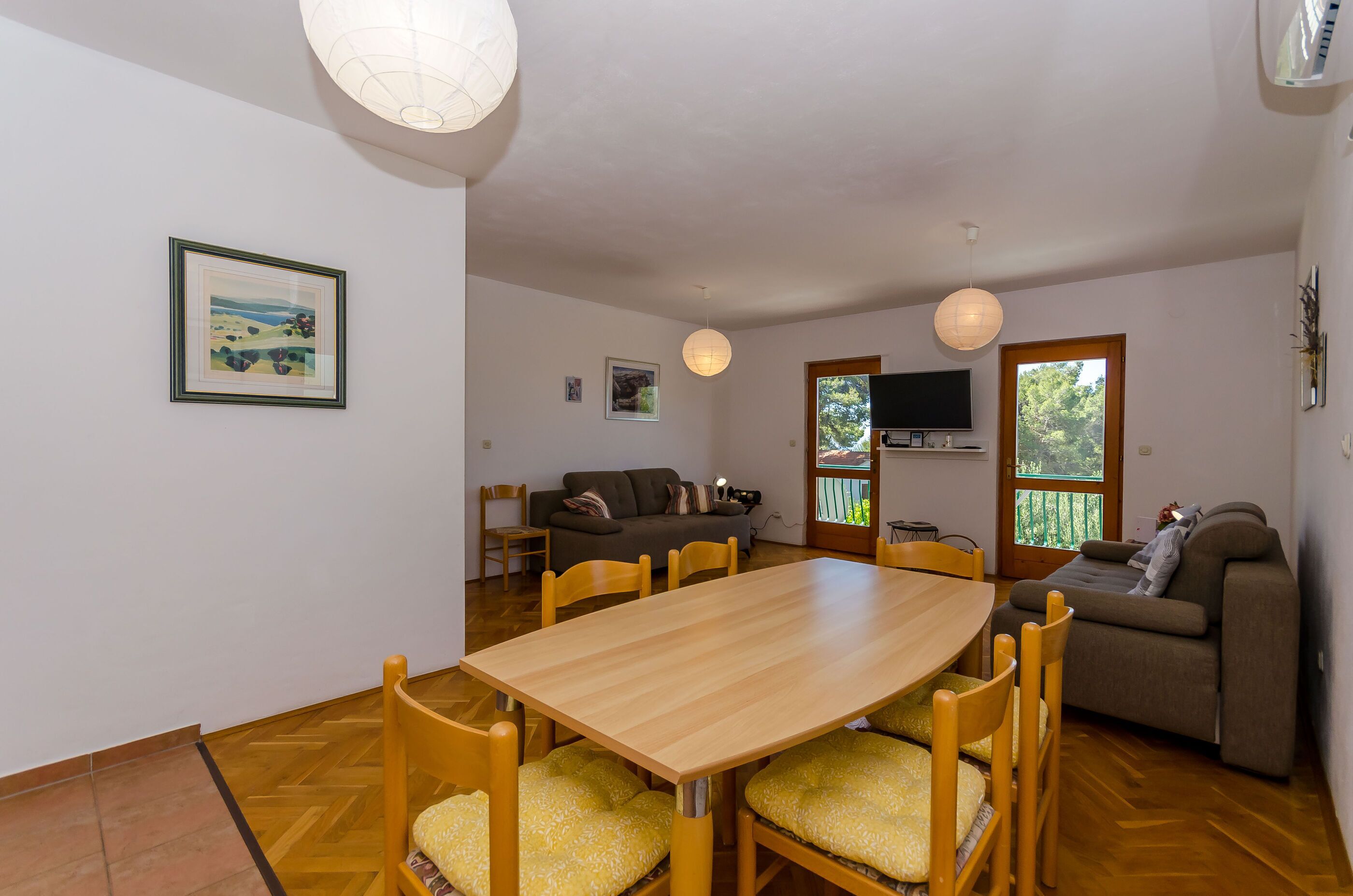 A dining area with a wooden table and chairs, a sofa, a TV, and a balcony door.