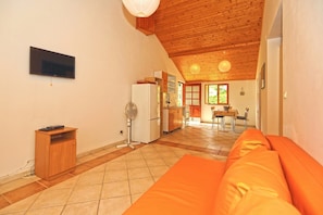 A kitchen with a refrigerator, stove, and wooden cabinets. There is a dining table with chairs and a window with a view of greenery. - Apartments Josip (Jelsa)