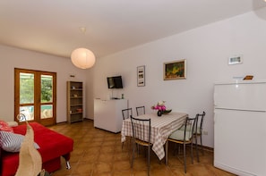 Ein kompakter Wohnbereich mit Essplatz, einem roten Sofa, einem Fernseher und einem Kühlschrank.