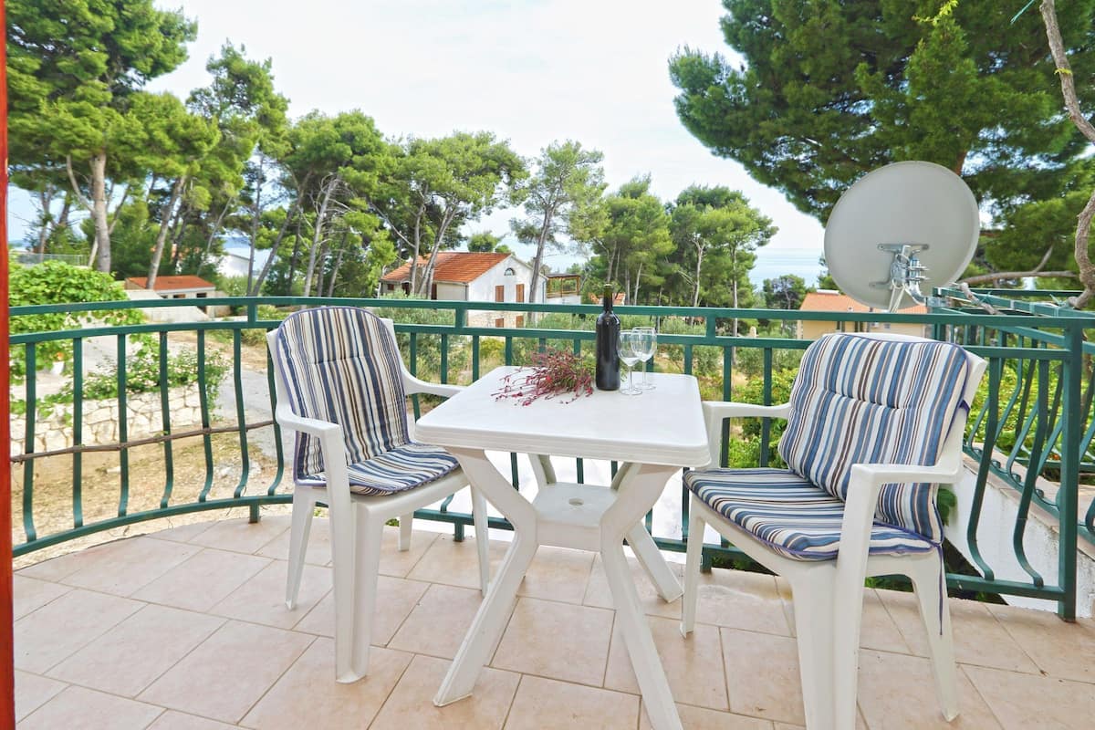 A patio with two striped chairs and a small table, a satellite dish, and a view of trees and a house.