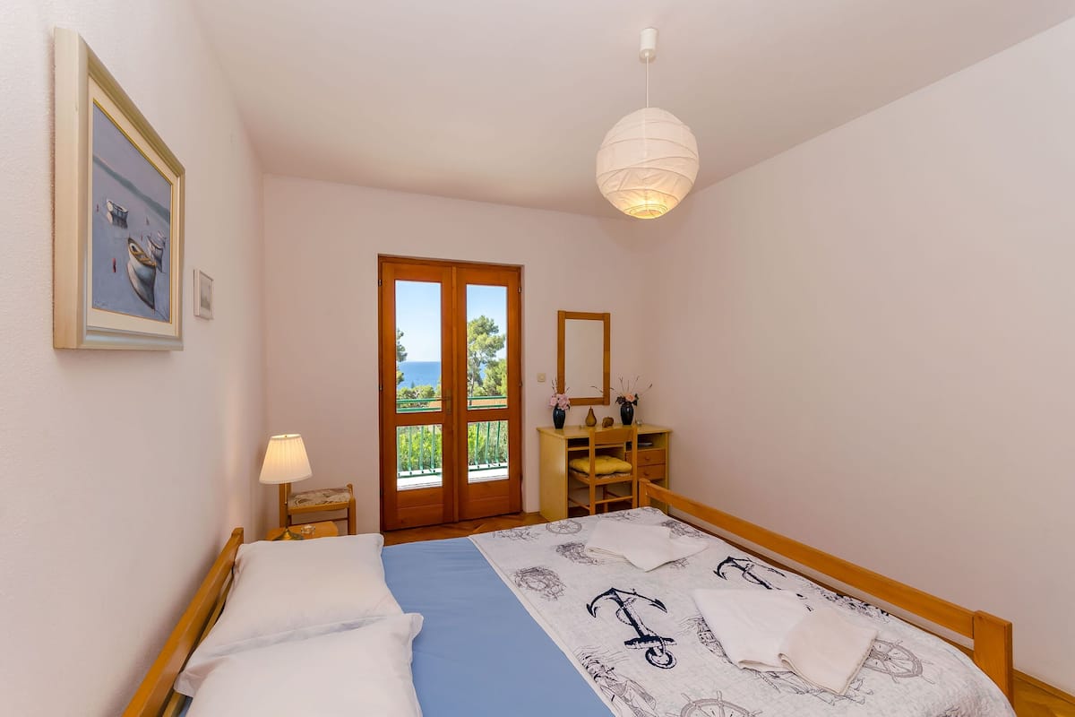 A bedroom with a bed, a nightstand, a lamp, a dresser, and a door leading to a balcony.