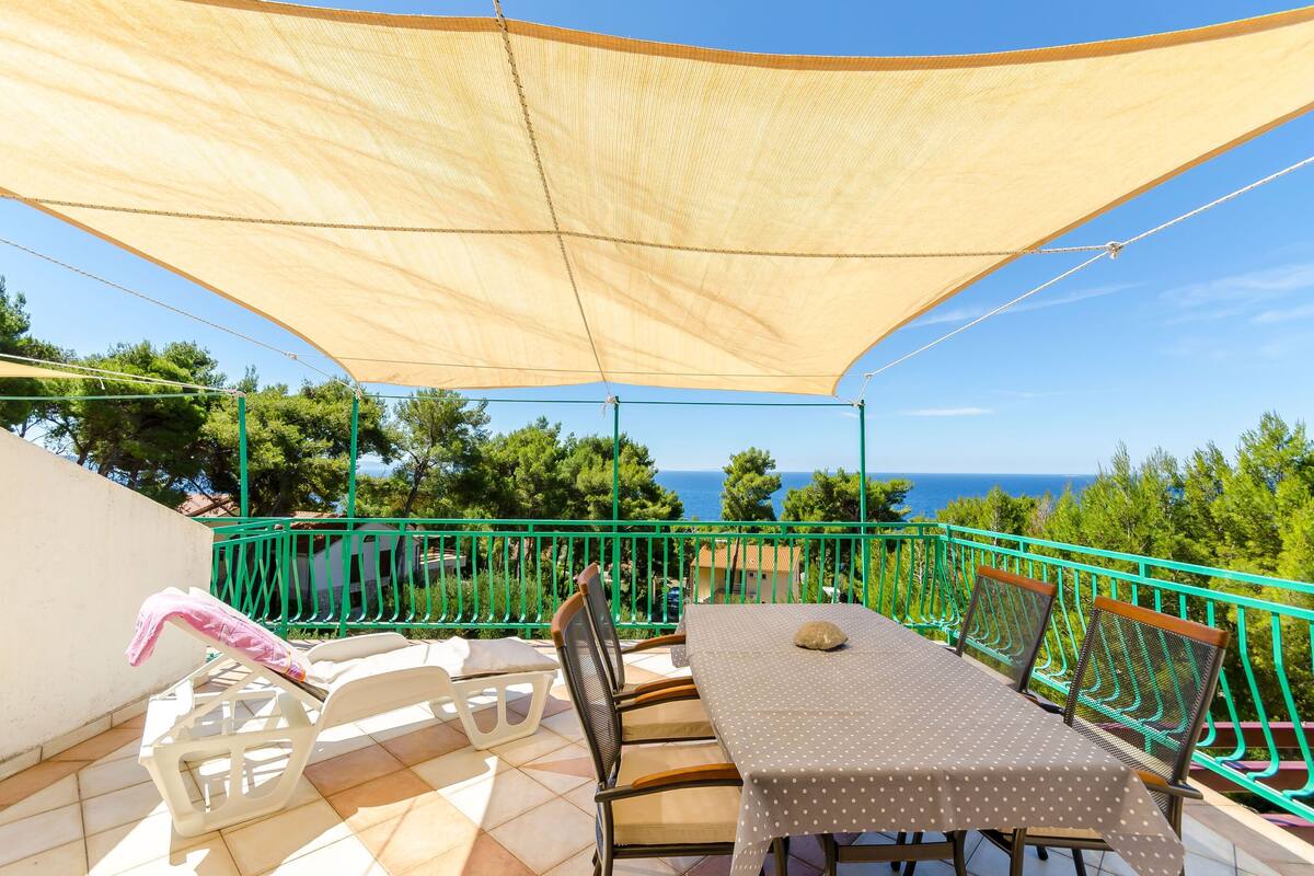 A terrace with a table and chairs, a sunshade, and a view of the sea.