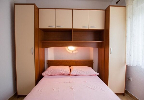 A bedroom with a bed, a wooden headboard, and a built-in wardrobe with multiple compartments. - Apartments Juri (Sucuraj)