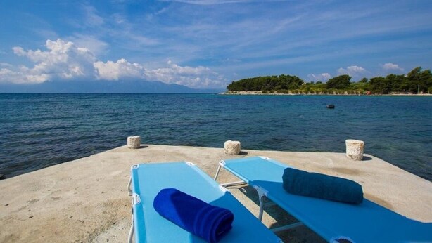 A beachside lounge with two blue sunbeds, a large blue umbrella, and a view of the sea and a distant island. - Apartments Juri (Sucuraj)