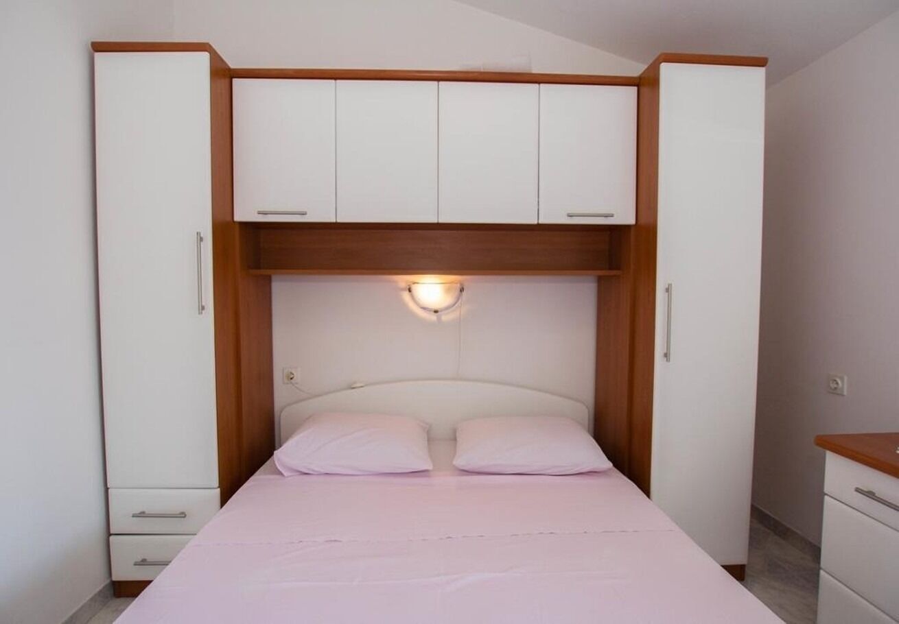 A bedroom with a bed, two white cabinets, a wooden headboard, and a wall-mounted light fixture.