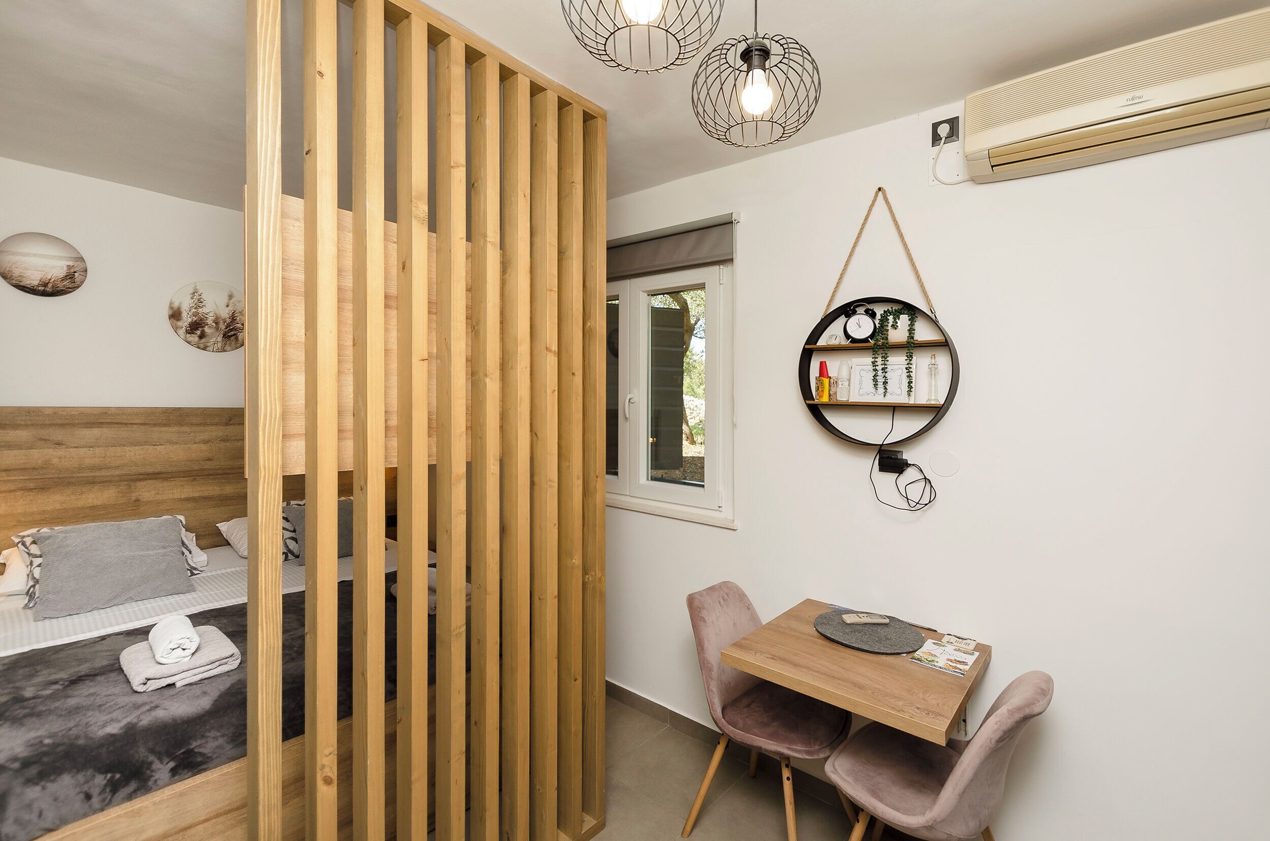 Une pièce comprenant un lit, une cloison en bois, une table avec des chaises, une horloge murale et un appareil de climatisation.