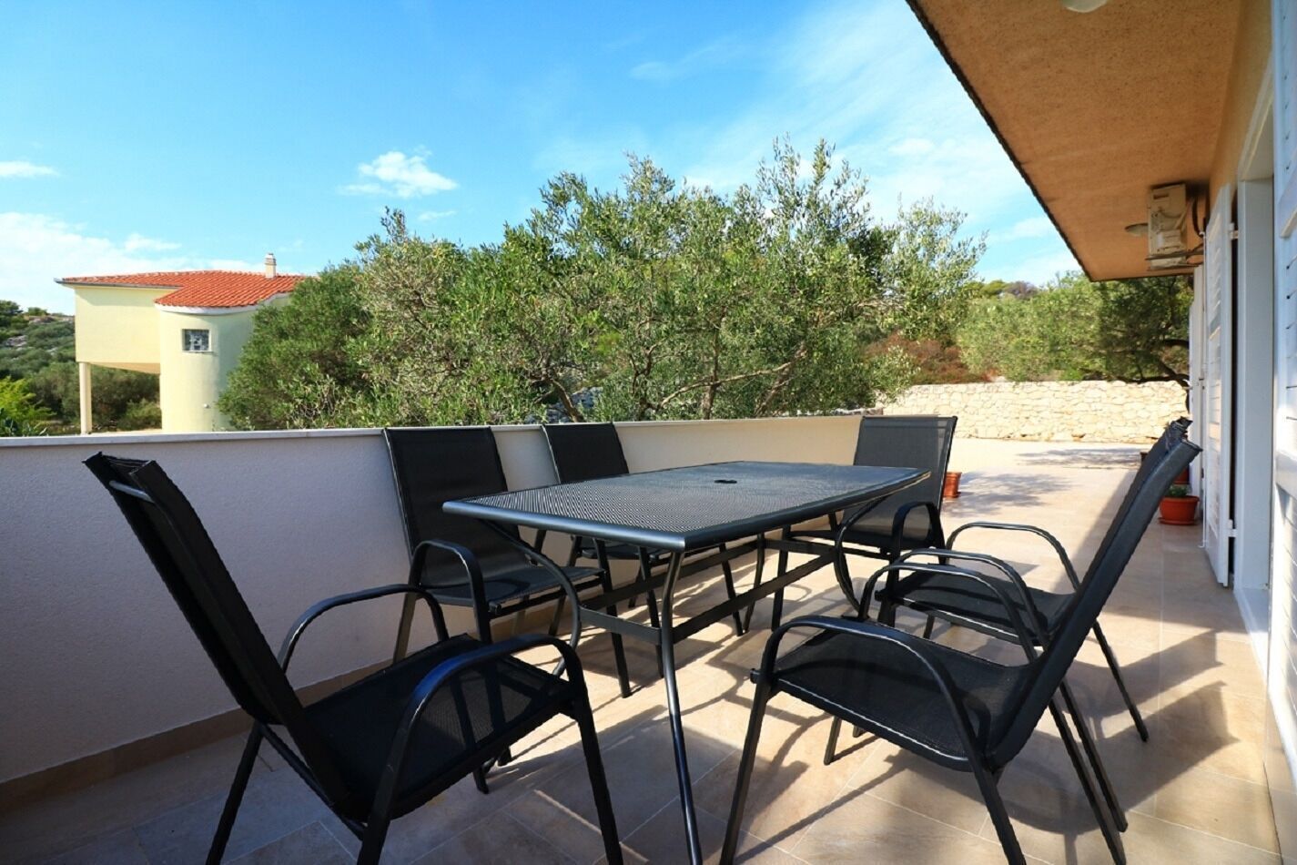 Een terras met een tafel en stoelen, een stenen muur en uitzicht op bomen en een gebouw op de achtergrond.