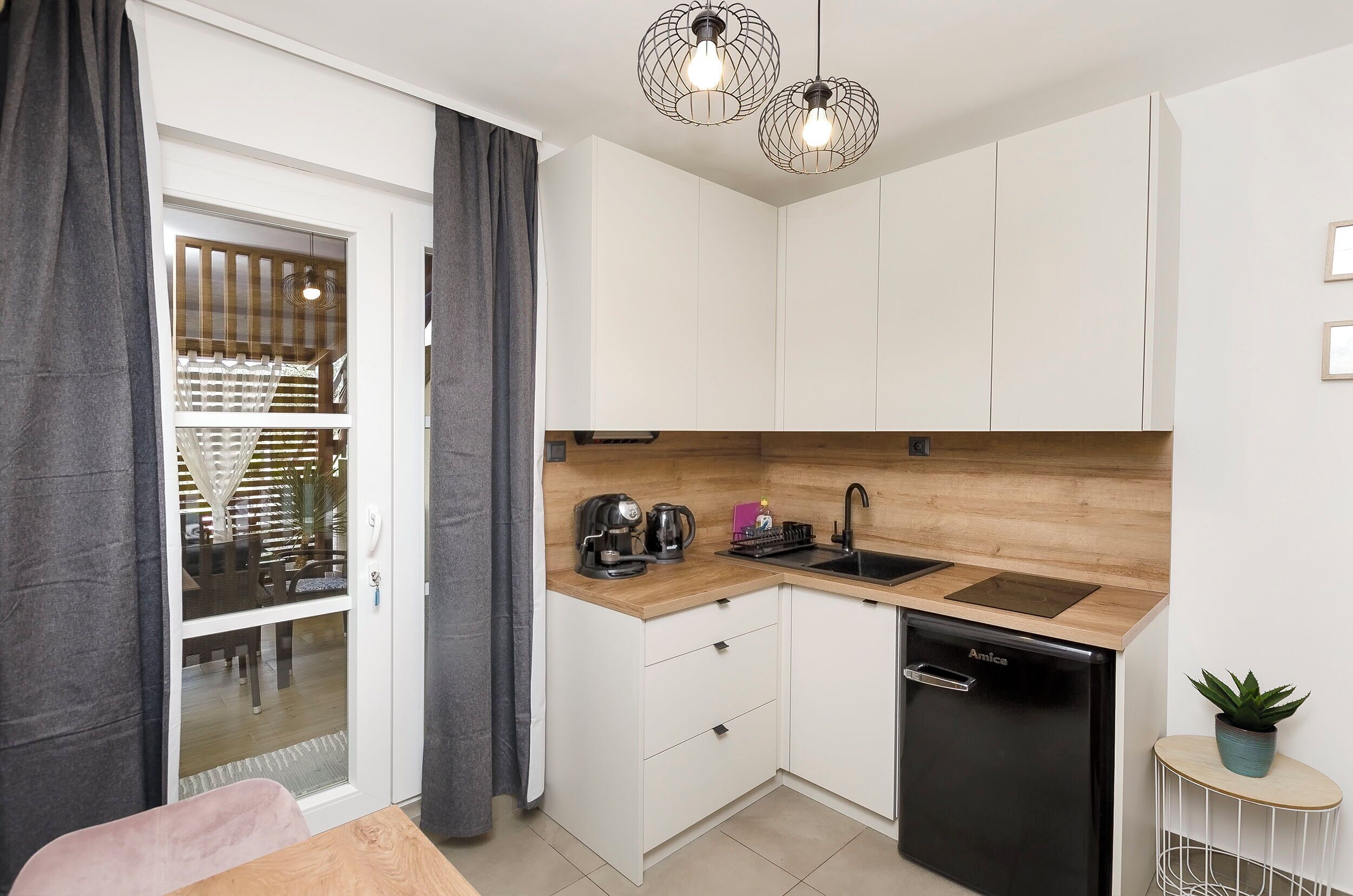 A compact kitchen with white cabinets, a black dishwasher, a coffee maker, and a small potted plant.