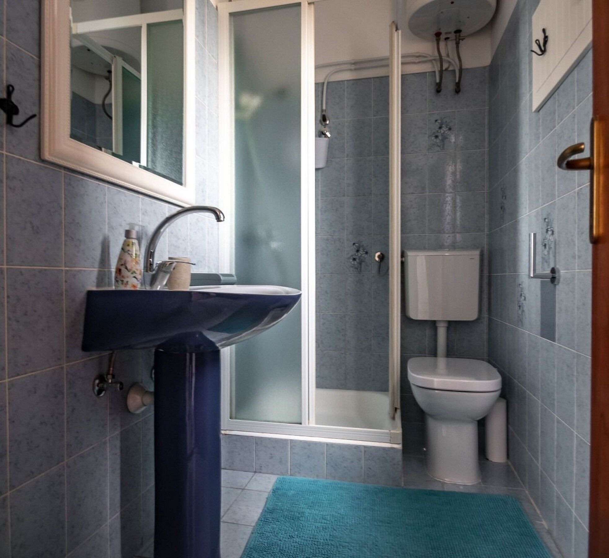 Une salle de bain avec un lavabo bleu foncé, des toilettes et une douche à parois de verre.