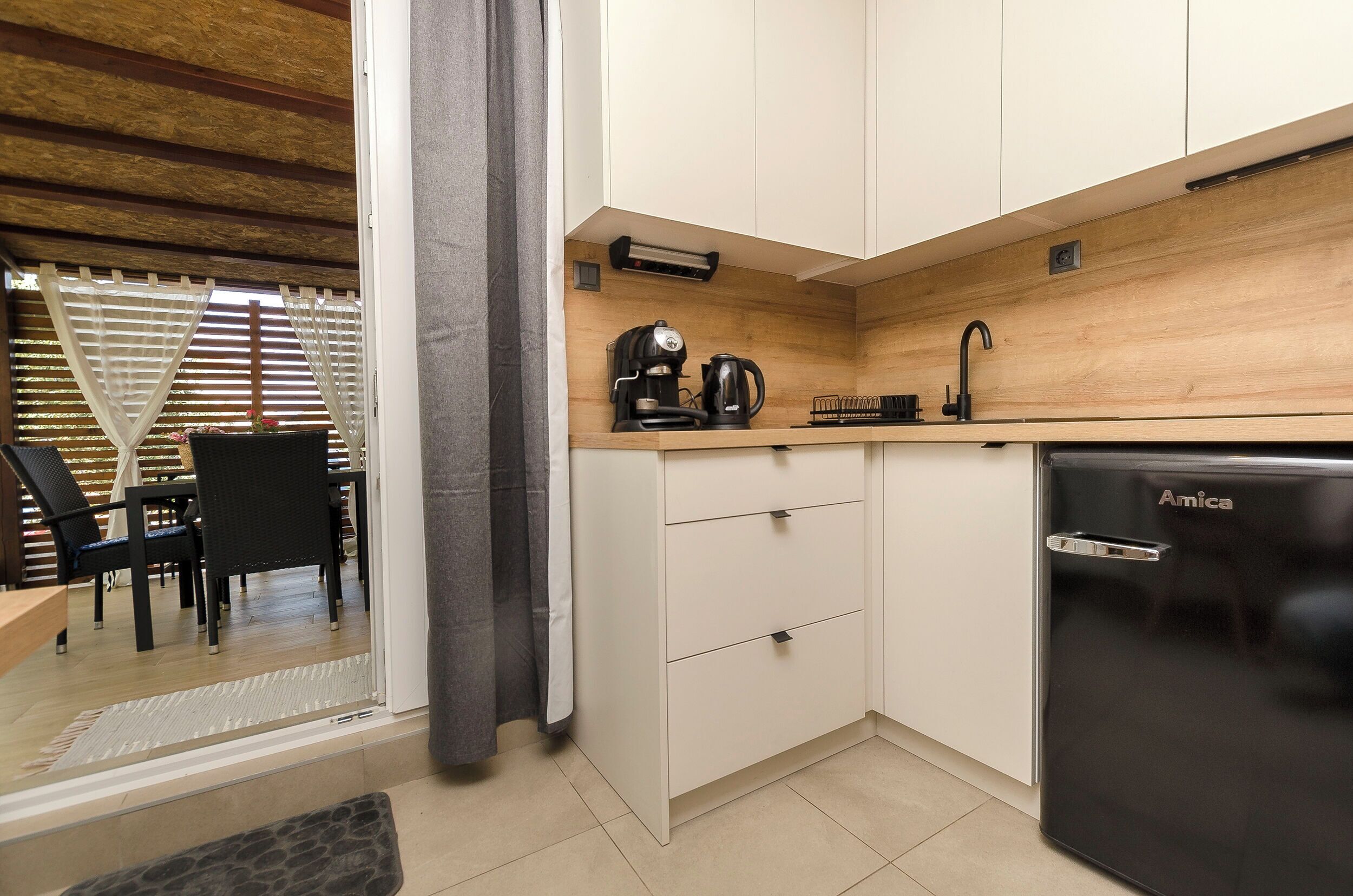 Cocina compacta con un refrigerador Amica negro, encimera de madera y armarios blancos.