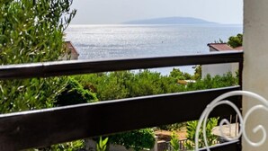 A balcony with a table and chairs, overlooking a body of water and greenery. - Apartments Goge (Gradac)