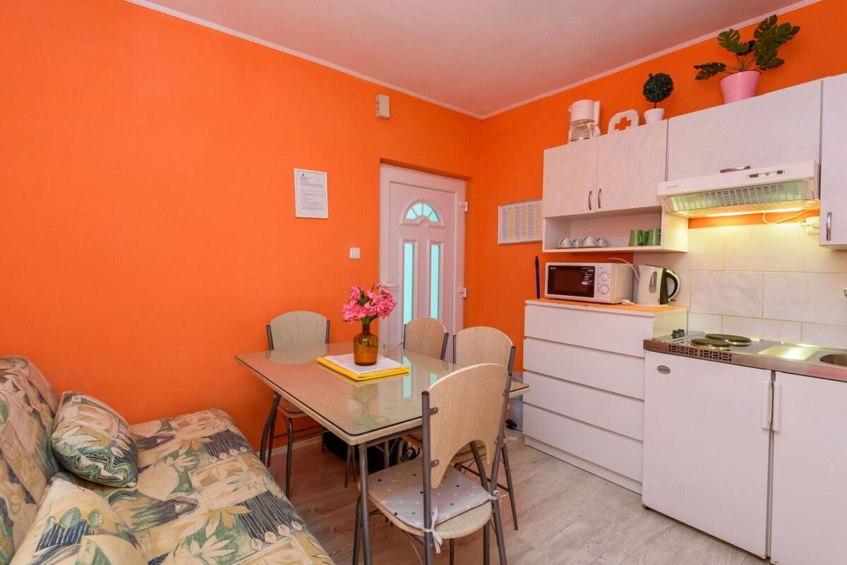 A compact kitchen with a microwave, kettle, and cabinets. There is a dining table with chairs and a sofa in the living area.