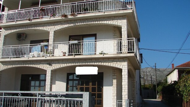 Ein zweistöckiges Gebäude mit einem Balkon im oberen Geschoss, einer Garagentür im Erdgeschoss und einem wolkenlosen Himmel im Hintergrund.