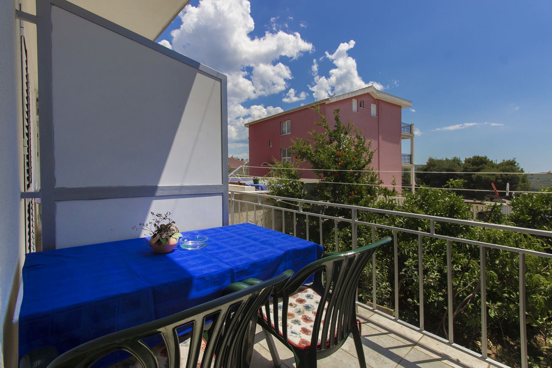 A balcony with a table and chair, a railing, and a red building in the background.