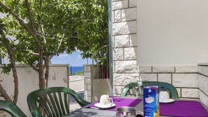 A table set outdoors with a metal pitcher, a box of fruit drinks, and a cup on a purple tablecloth. - Apartments Vinko (Primosten)
