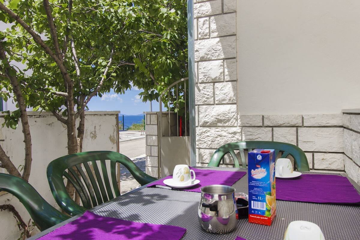 Une table dressée à l’extérieur, avec un pichet en métal, une boîte de jus de fruits et une tasse posée sur une nappe violette.
