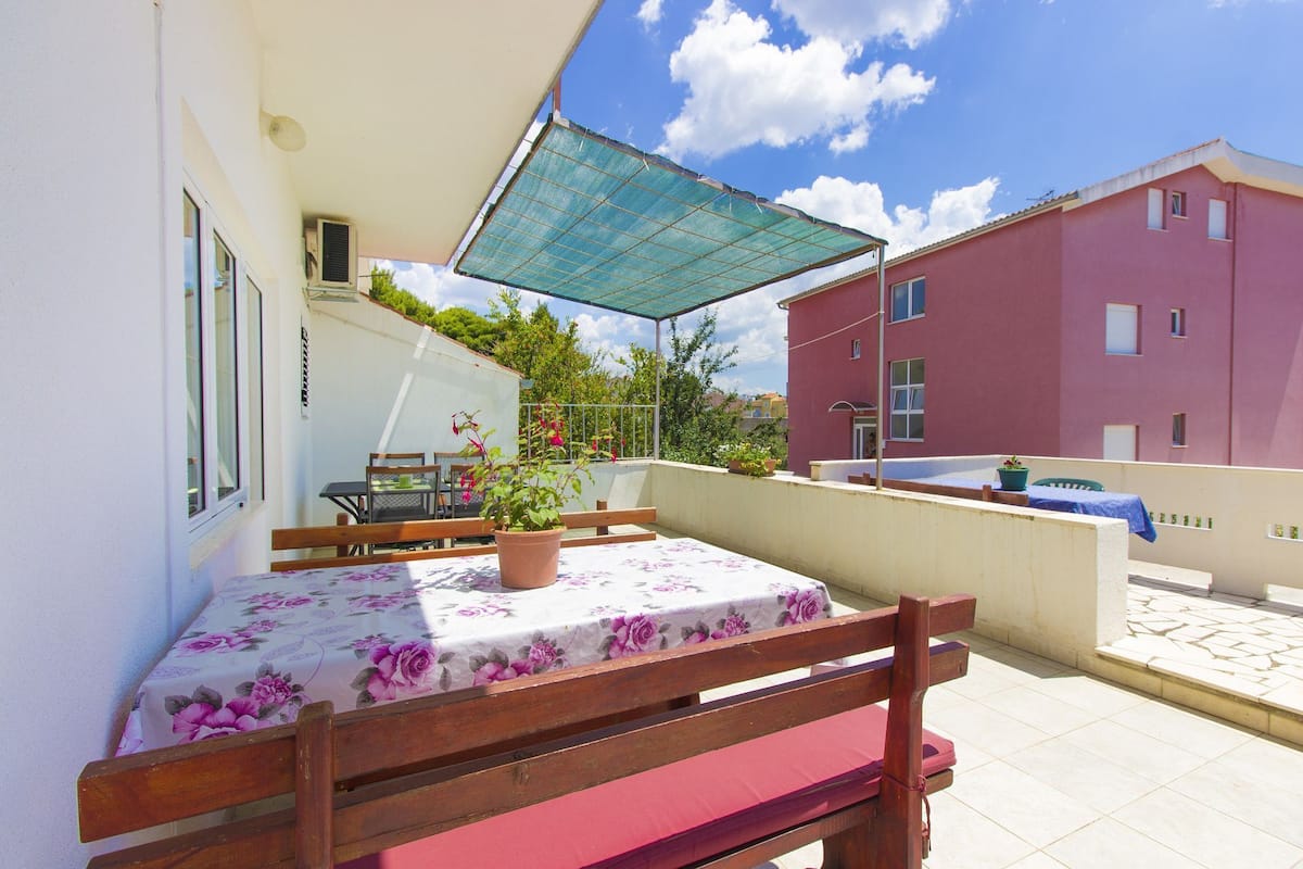 Un balcon avec une table et des chaises, un pot de fleurs et un auvent bleu.