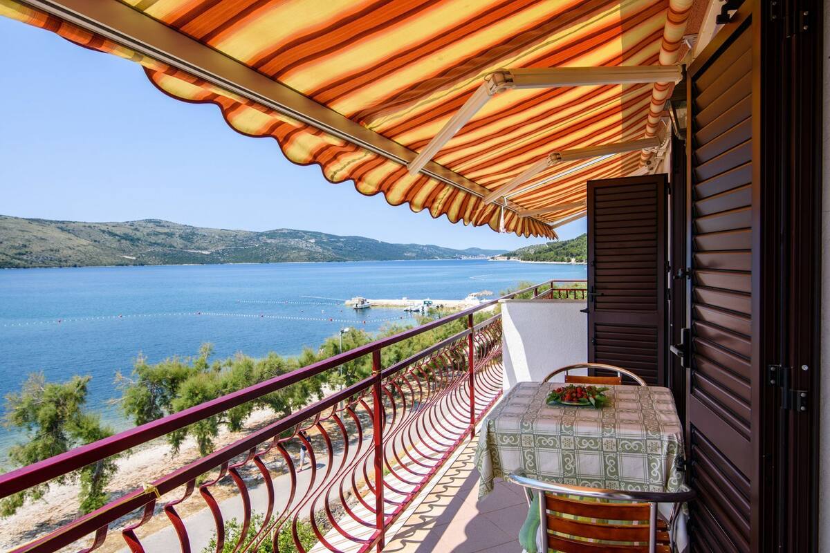 A balcony with a view of a lake, a table with a tablecloth, and a chair.