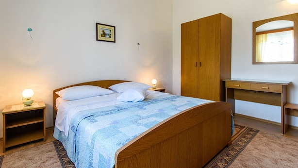 Ein Schlafzimmer mit einem Holzbett, Nachttischen mit Lampen, einem Holzschrank, einem Schreibtisch mit Spiegel und einem gerahmten Bild an der Wand.