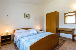 Ένα υπνοδωμάτιο με ένα ξύλινο κρεβάτι, κομοδίνα με φωτιστικά, μια ξύλινη ντουλάπα, ένα γραφείο με έναν καθρέφτη και έναν πίνακα με κορνίζα στον τοίχο.