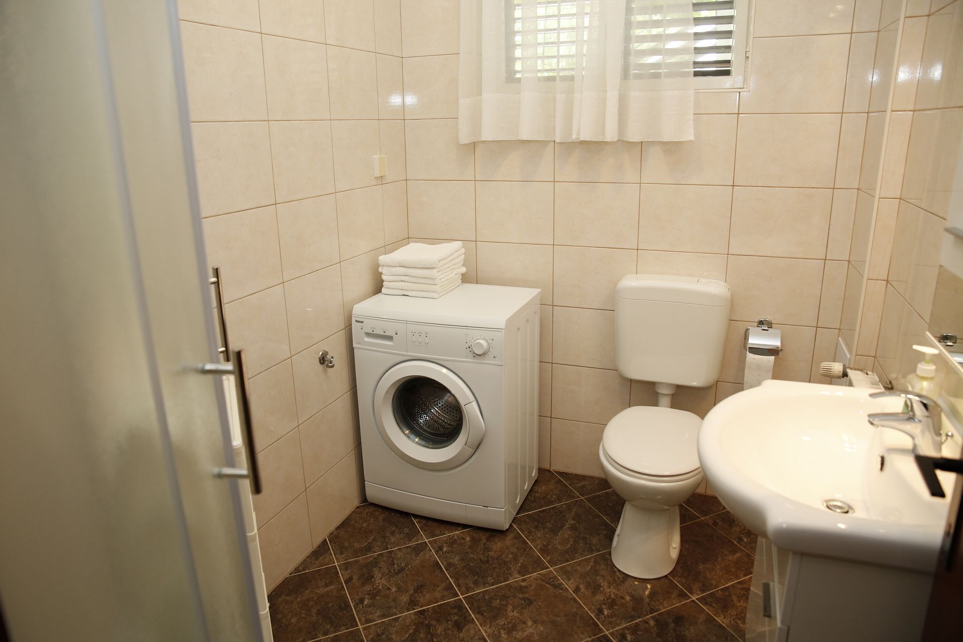 A compact bathroom with a washing machine, toilet, and sink.