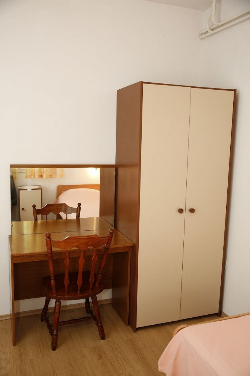 A room with a wooden desk, a chair, a wardrobe, and a bed.