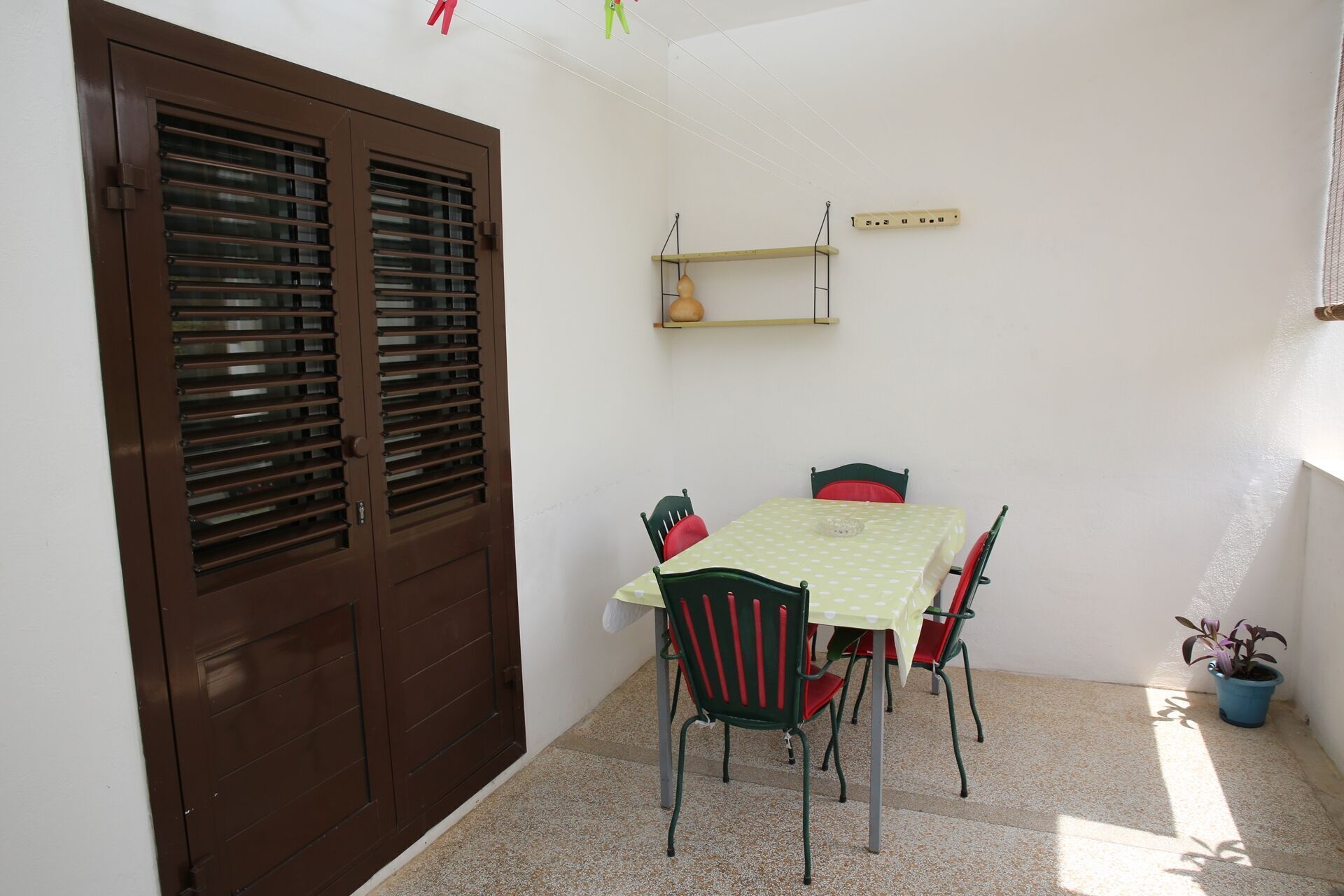 Un pequeño comedor con una mesa y sillas, una puerta marrón con paneles de vidrio listonados, una repisa con una bombilla y una planta en maceta.