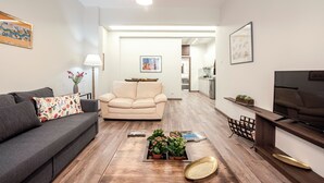 Un salon moderne avec un canapé gris, un fauteuil beige, une table basse en bois et un téléviseur posé sur un meuble en bois.