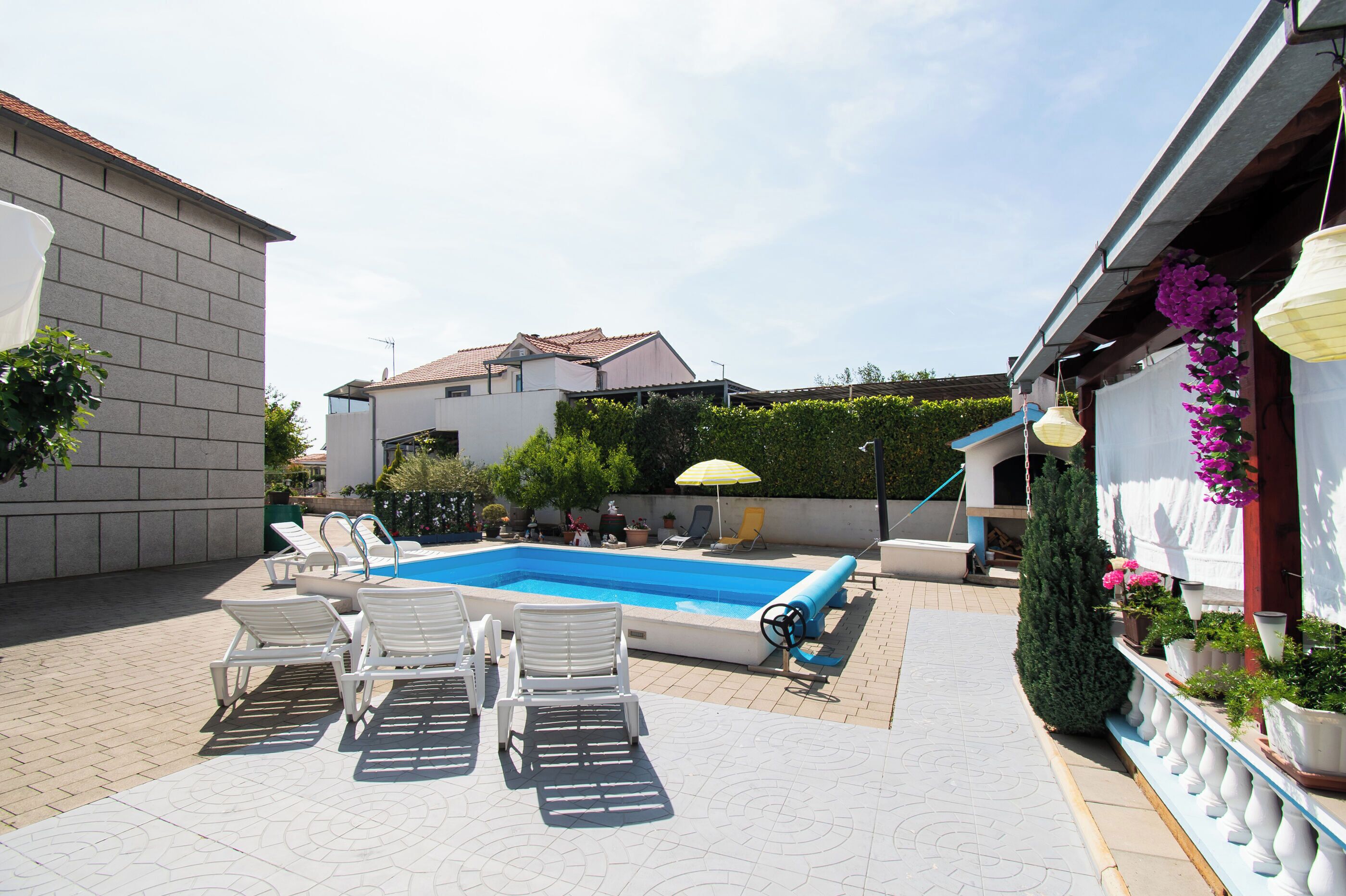 Piscina con sillones de descanso, una sombrilla y plantas en macetas.