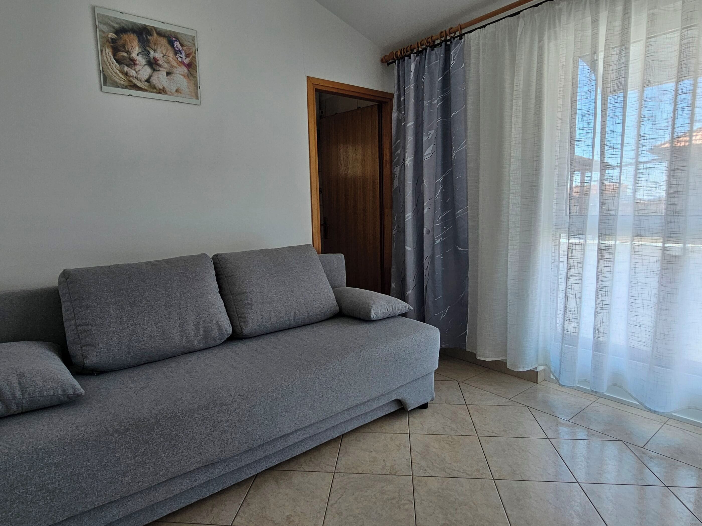 Ein graues Sofa, eine Tür und ein Fenster mit Vorhängen.