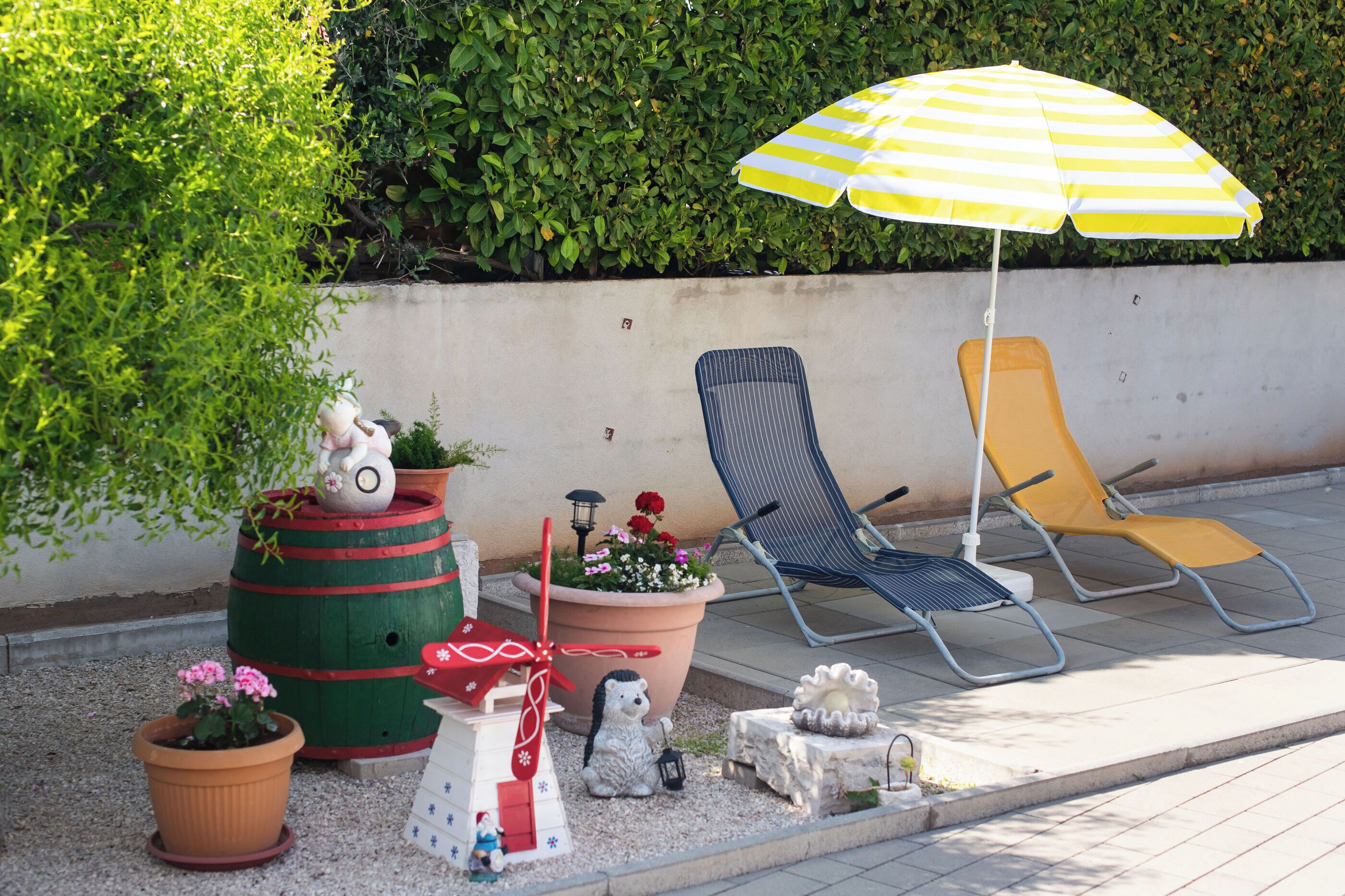 Un'area patio con piante in vaso, un ombrellone a righe e due poltrona relax.