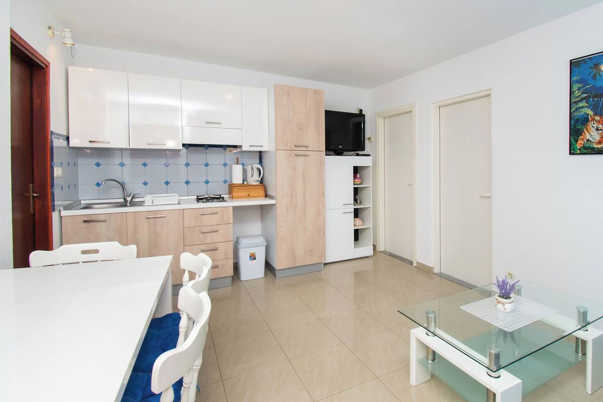 A modern kitchen with white cabinets, a microwave, and a coffee maker. There is a glass table with a vase of flowers.