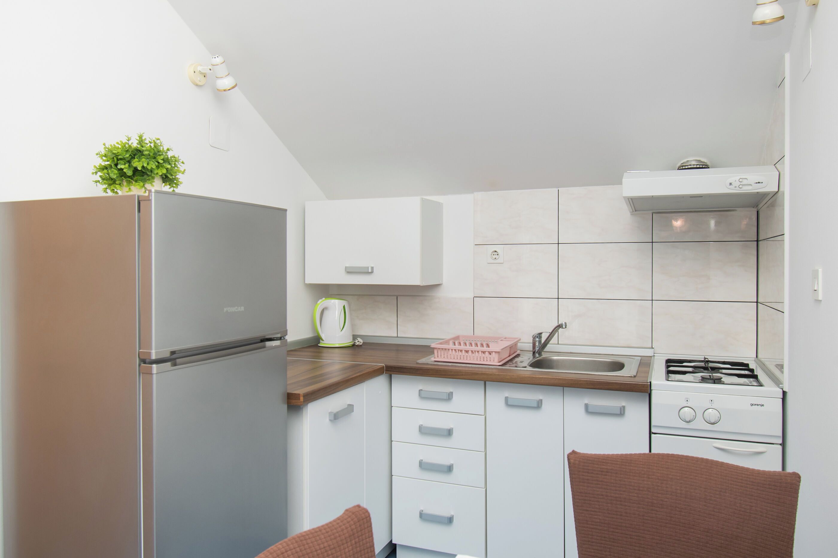 Een kleine keuken met een koelkast, fornuis, spoelbak en witte kastjes.
