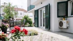 A patio with a seating area, a potted plant, and a wall-mounted air conditioning unit. - Apartments Petri (Tisno)